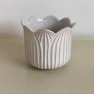 Può includere: Vaso in ceramica bianca con bordo ondulato e design a coste. Il vaso ha una smaltatura marrone chiaro.