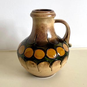 Könnte beinhalten: Eine braune Keramikvase mit einem geometrischen Muster in Grün und Orange. Die Vase hat einen Henkel und einen runden Körper.