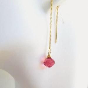 May include: A gold-tone threader earring featuring a delicate chain that suspends a faceted, teardrop-shaped pink gemstone. The gemstone is secured with gold wire wrapping at the top, and the earring includes a straight, thin metal post.