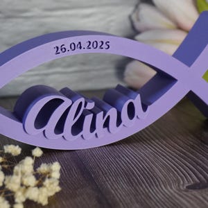 May include: A purple wooden fish-shaped sign with the name "Alina" and the date "26.04.2025" engraved on it.