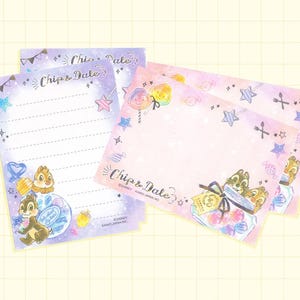 May include: A set of four pink and blue stationery notepads featuring Chip and Dale, characters from Disney's animated film, Chip 'n Dale Rescue Rangers. The notepads have a whimsical design with candy, stars, and hearts. The text "Chip & Dale" is printed on the front of the notepads.