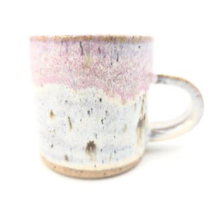 May include: A white ceramic mug with a black handle and the text "But first, coffee" in a black, handwritten-style font. The mug is on a wooden surface.