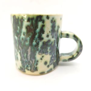 May include: A ceramic mug with a speckled glaze in shades of green, teal, and cream. The mug has a rounded body and a curved handle. The speckled pattern gives the mug a unique, handcrafted appearance.