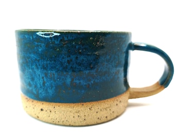 Op de afbeelding: Een handgemaakte keramische mok met een blauw glazuur en een bruine basis. De mok heeft een afgeronde vorm met een oor en is geschikt voor warme of koude dranken. De mok is ongeveer 10 cm hoog.