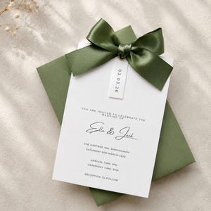 Puede incluir: Una tarjeta de invitaci&oacute;n de boda blanca con texto negro que dice Ella & Jack, The Oaktree Inn, Birmingham, Saturday 3rd March 2026, y una peque&ntilde;a etiqueta con 03.03.26, rematada con un lazo de sat&eacute;n verde oliva oscuro sobre un sobre verde a juego.