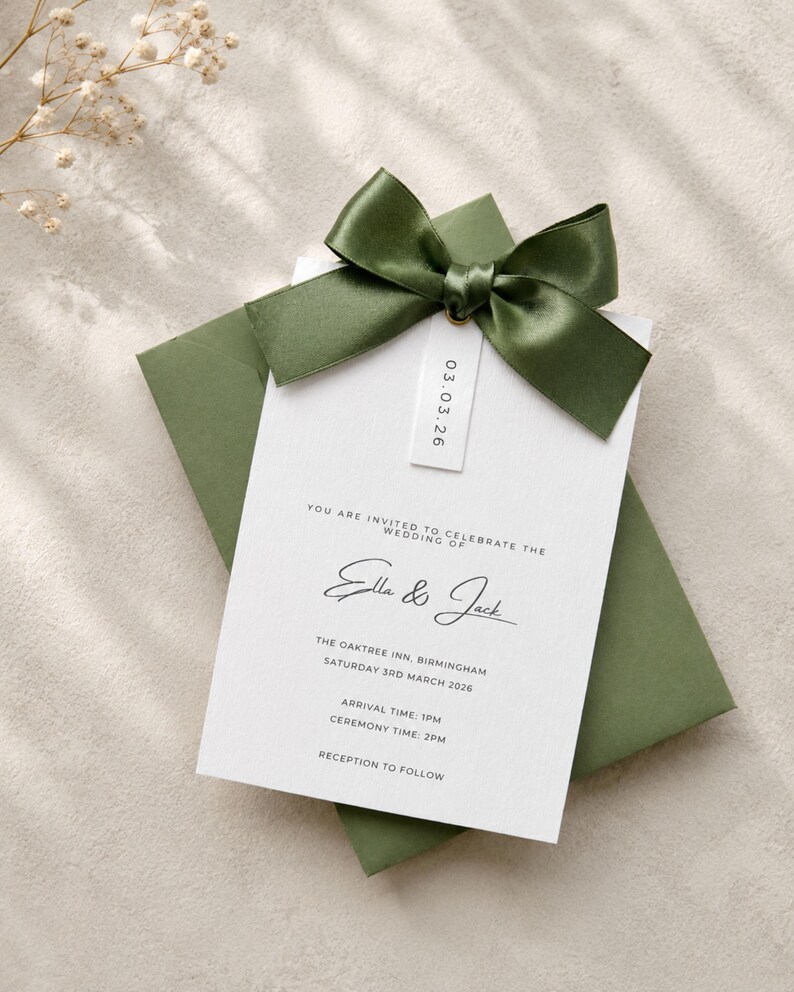 Puede incluir: Una tarjeta de invitaci&oacute;n de boda blanca con texto negro que dice Ella & Jack, The Oaktree Inn, Birmingham, Saturday 3rd March 2026, y una peque&ntilde;a etiqueta con 03.03.26, rematada con un lazo de sat&eacute;n verde oliva oscuro sobre un sobre verde a juego.