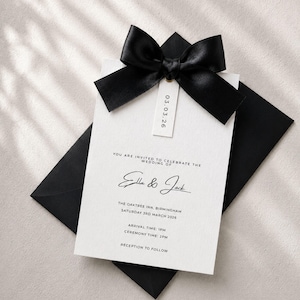 Puede incluir: Una tarjeta de invitaci&oacute;n de boda blanca con texto negro y un lazo de sat&eacute;n negro. Una peque&ntilde;a etiqueta vertical unida al lazo muestra la fecha 03.03.26. El texto dice: You are invited to celebrate the wedding of Ella & Jack, The Oaktree Inn, Birmingham, Saturday 3rd March 2026, Arrival time: 1pm, Ceremony time: 2pm, Reception to follow.