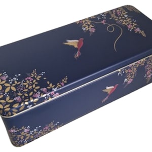 Puede incluir: Una caja rectangular de metal azul marino con un diseño floral y dos pájaros rojos. Los pájaros están volando y tienen detalles dorados. La caja tiene un borde dorado alrededor de los bordes.