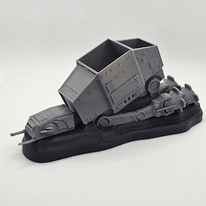 May include: A grey 3D printed model of a Star Wars Imperial Troop Transport, also known as a 'TIE' transport, with a black base. The transport is tilted on its side, with the cargo bay doors open.