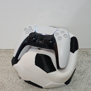 May include: A white PlayStation 5 controller resting on a white and black football.