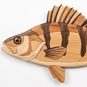 May include: A decorative wall hanging shaped like a fish, crafted from multiple pieces of wood in varying shades of light tan, medium brown, and dark brown. The design features vertical stripes, a detailed eye, and segmented fins and tail.