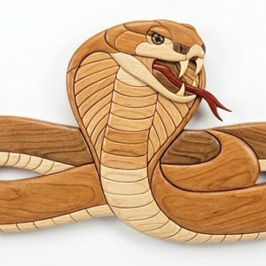 May include: A wooden intarsia wall art piece depicting a cobra snake in a coiled position. The sculpture features various shades of natural wood grain, including light cream and medium brown tones, with a red wooden tongue and white fangs.