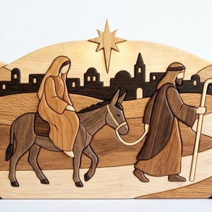 May include: A multi-layered wooden wall art piece depicting a nativity scene with a figure riding a donkey and another figure walking with a staff. The scene features a desert landscape, a distant town silhouette, and a star at the top center.