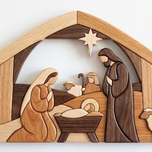 May include: A wooden nativity scene wall art piece crafted from various shades of light and dark wood. The design features a stable structure, a star, and figures of a kneeling person, a standing person, a baby in a manger, and two sheep.