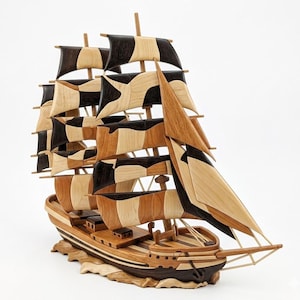 May include: A wooden model of a tall ship with sails. The ship features a detailed design with alternating black, light, and medium brown wood pieces. The sails are intricately crafted, and the ship sits on a wooden base.