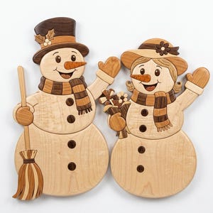 May include: Wooden snowman couple wall art. The male snowman wears a top hat and holds a broom, while the female snowman has a hat with a flower and holds flowers. Both have carrot noses, scarves, and mitten-clad hands.