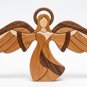 May include: A decorative wooden angel figurine crafted from multiple shades of natural wood. The figure features a circular halo, outstretched wings with layered segments, and a flowing gown design, all assembled from light and dark wood pieces.