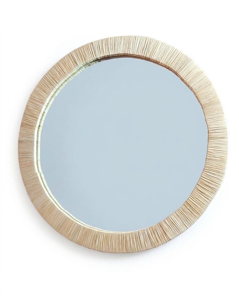 May include: A circular wall mirror featuring a wide frame constructed from tightly arranged, light beige natural fibers. The reflective glass surface is smooth and clear, centered within the textured, straw-like border that radiates outward.