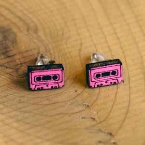 May include: A pair of pink cassette tape earrings. The earrings are made of wood and have a black outline.