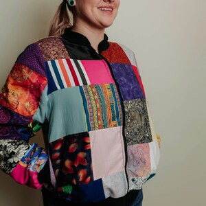 Può includere: Una giacca bomber colorata in patchwork con chiusura a zip. La giacca è realizzata con diversi tessuti e motivi, tra cui disegni floreali, geometrici e a righe.