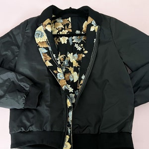 May include: A black reversible bomber jacket with a floral print lining. The jacket has a zipper closure and ribbed cuffs and hem.