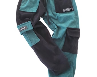 Könnte beinhalten: Cordhose in Teal und Schwarz mit mehreren Taschen und einem Kordelzug in der Taille. Die Hose hat den Text "R Gnarly" am Bündchen und "OHZIGGY" auf einem Aufnäher. Hergestellt aus weichem Cordstoff.