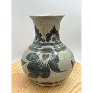 May include: A ceramic vase with a bulbous body and a flared rim, featuring a light beige base color with hand-painted dark gray floral motifs and horizontal bands encircling the neck and base, finished with a glossy, smooth, reflective glaze.