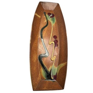 Può includere: Un piatto rettangolare in ceramica con base marrone e design decorativo. Il design include una linea ondulata nera, argentata e dorata, con accenti rossi e verdi. Il piatto ha una finitura lucida.