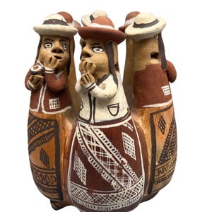 May include: A ceramic sculpture of three figures in hats and traditional attire. The figures have surprised expressions, with hands near their faces. The sculpture is painted in brown, red, and white, with detailed patterns on the clothing.
