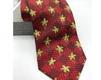 May include: A red tie with a repeating pattern of yellow flowers and red accents. The tie has a textured, geometric background. The tie is folded over a gray box.