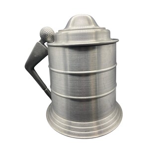 May include: A silver-colored beer stein with a lid and handle. The handle is shaped like a golf club, and the lid is topped with a golf ball. The stein has a cylindrical body with horizontal bands.