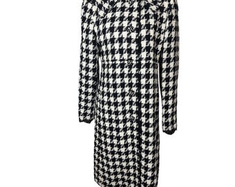 May include: A black and white houndstooth pattern coat with a collared neckline and button closure. The long coat has long sleeves and a tailored fit, suitable for cooler weather. The coat is displayed on a mannequin.
