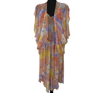 May include: A sleeveless midi dress featuring a sheer, draped overlay with a watercolor floral print in shades of orange, yellow, and purple. The garment has a scoop neckline, a loose, flowing silhouette, and a lightweight, semi-transparent fabric.