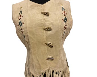 Puede incluir: Chaleco de ante beige con costuras decorativas y cierres de palanca de madera. El chaleco presenta flecos a lo largo del dobladillo inferior y patrones geométricos bordados en tonos rojos, verdes y azules. Una pieza vintage elegante.