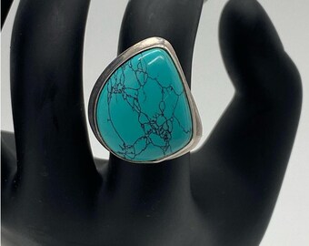 Könnte beinhalten: Silberring mit einem großen, tropfenförmigen Türkisstein mit schwarzen Adern. Der Stein ist in eine silberne Lünette gefasst. Dieser Statement-Ring ist ideal, um jedem Outfit einen Farbtupfer zu verleihen.