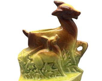 Może przedstawiać: Wazon ceramiczny w stylu vintage z motywem jelenia i sarny. Wazon jest głównie brązowy i żółty, z błyszczącym wykończeniem. Jeleń stoi, a sarna jest obok niego. Podstawa jest prostokątna i pomalowana na jasnozielony kolor.