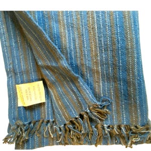 May include: A blue and brown striped woven textile with white accents and fringe. The textile is made of cotton and has a tag attached. The stripes run vertically, and the fringe is at the bottom.