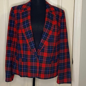 Puede incluir: Un blazer a cuadros rojos, azules y verdes. El blazer tiene un cierre de un solo botón y dos bolsillos delanteros. El patrón de cuadros es un diseño clásico, perfecto para un look vintage o preppy.