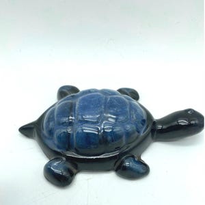 Puede incluir: Figura de tortuga de cerámica con acabado brillante. El caparazón de la tortuga es azul oscuro, mientras que el cuerpo, la cabeza y las extremidades son negros. La figura es un objeto decorativo, probablemente para exhibición.