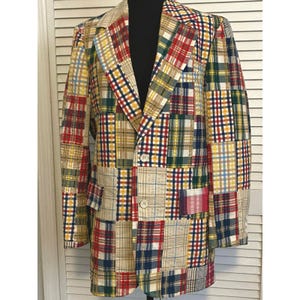 Könnte beinhalten: Ein Patchwork-Blazer mit einer lebendigen Mischung aus karierten Mustern in Rot, Gelb, Grün, Blau und Beige. Der Blazer hat ein fallendes Revers, zwei Knöpfe und zwei Vordertaschen. Das Kleidungsstück wird auf einer schwarzen Schaufensterpuppe präsentiert.