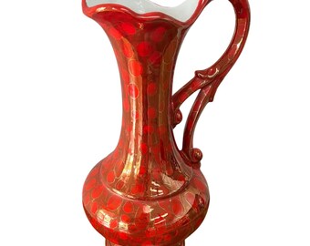 May include: A decorative red and gold ceramic pitcher with a large handle and a wide, ruffled rim. The pitcher is adorned with a pattern of red circles and has a white interior.