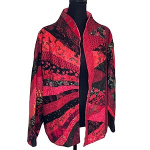 May include: A patchwork jacket in shades of red and black. The jacket features a variety of fabric patterns, including floral, star, and geometric designs. The open-front jacket has a collar and long sleeves. The jacket is displayed on a black mannequin.