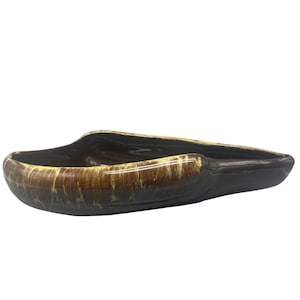 Könnte beinhalten: Ein brauner und gelber Keramik-Aschenbecher in Bootsform. Der Aschenbecher hat eine glänzende Oberfläche und eine dunkelbraune Außenseite mit einer helleren braunen und gelben Innenseite.
