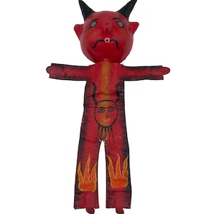 Puede incluir: Una figura de diablo roja con cuernos negros, ojos verdes y una boca pequeña. El torso presenta una cara negra pintada a mano con cuernos, mientras que las piernas muestran diseños de llamas amarillas y naranjas. Cuerpo plano y alargado.
