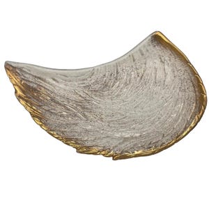 May include: A decorative, wing-shaped dish with a textured, off-white interior and a gold-colored rim. The dish has a unique, organic shape and is likely made of glass or a similar material. The gold rim adds a touch of elegance.