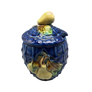 May include: A blue ceramic jar with a lid, featuring a pear-shaped knob. The jar is decorated with a pear and leaf motif in shades of green, brown, and yellow. The jar has a textured surface.