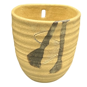 Puede incluir: Un jarrón de cerámica hecho a mano con un exterior texturizado de color beige y un diseño abstracto gris oscuro. El jarrón tiene una forma única con una pequeña abertura rectangular cerca de la parte superior. El diseño incluye un remolino y trazos verticales.
