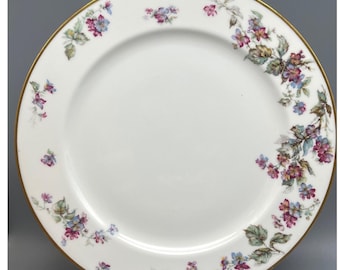 Peut inclure: Assiette en porcelaine blanche avec un bord doré et un motif floral. L'assiette présente un motif délicat de fleurs roses, violettes et bleues avec des feuilles vertes. Les fleurs sont disposées en un motif gracieux et incurvé.