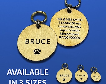 May include: Two round gold-toned metal pet tags with split rings. One tag shows the name BRUCE and a paw print. The other shows MR & MRS SMITH, an address, and contact details. Text at the bottom reads AVAILABLE IN 3 SIZES with Large, Medium, and Small tags.