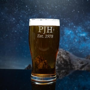 May include: A pint glass filled with amber beer and a white head. The glass is engraved with the initials "PJH" and the year "Est. 1978". The background shows a starry night sky and a mountain range, creating a scenic backdrop.